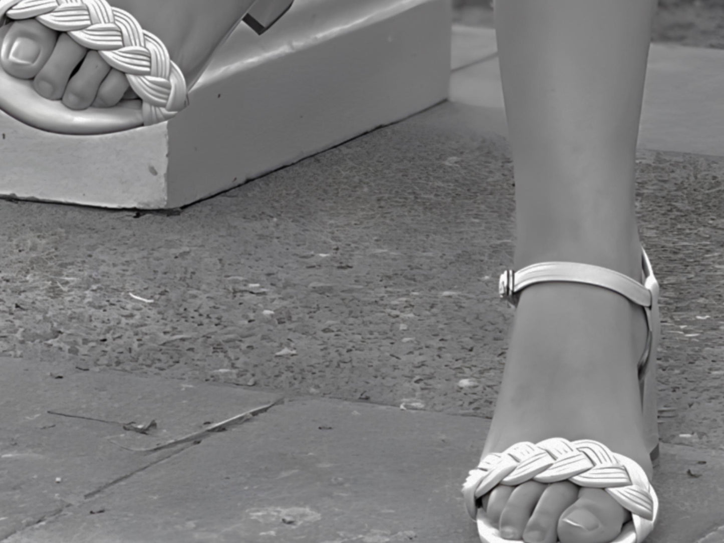 Close-up of a foot wearing a sandal with a woven design on a concrete surface.