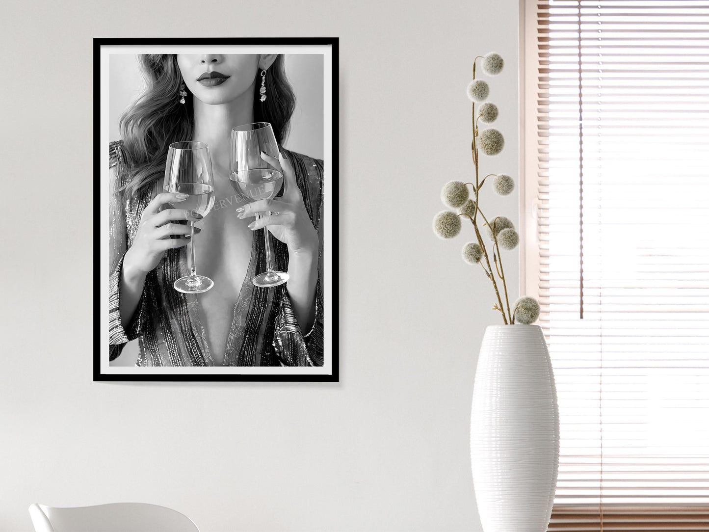 Framed artwork of a woman holding wine glasses on a wall next to a white vase with dried flowers.