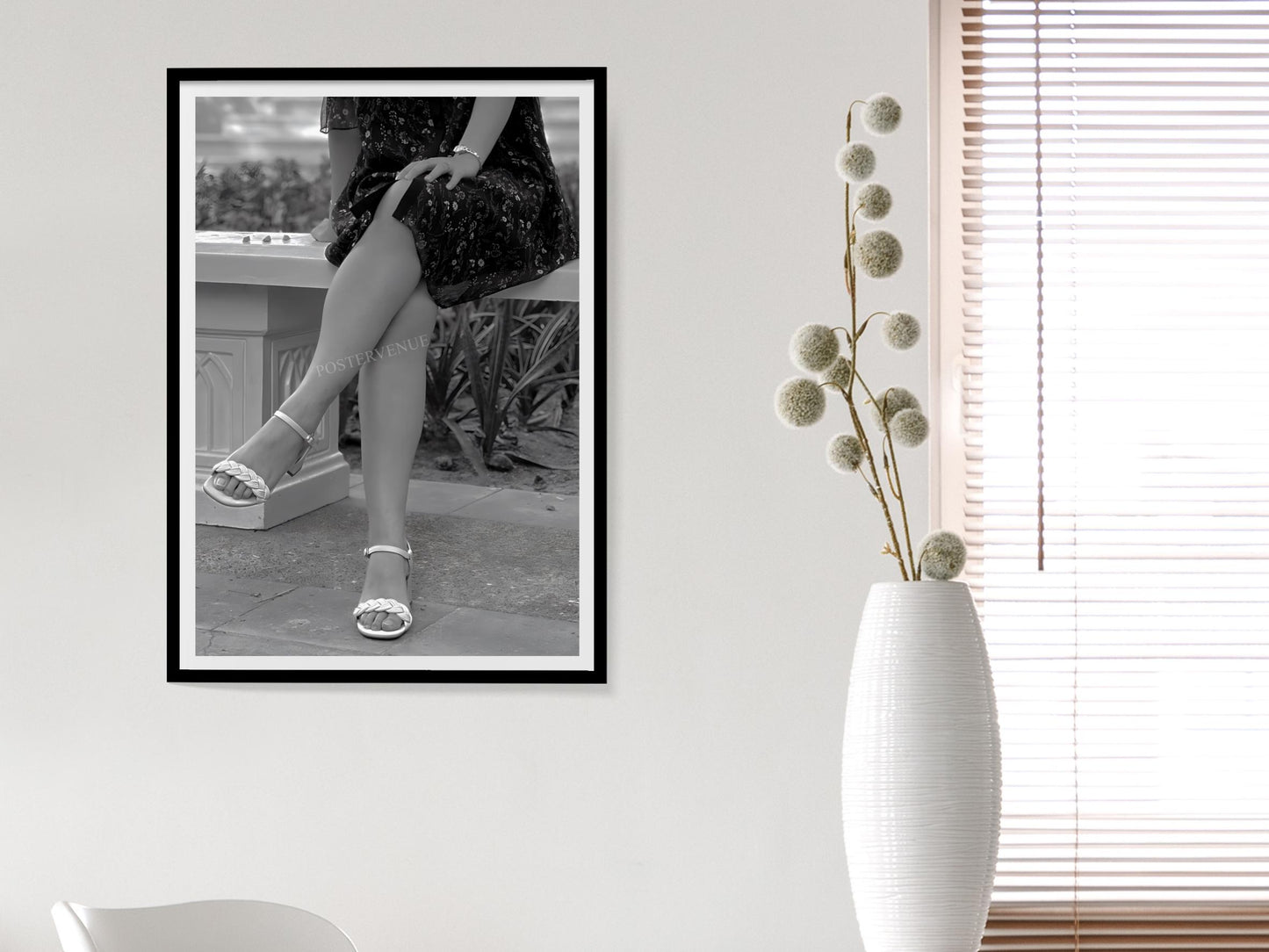 Framed black and white photo of a person in high heels on a wall next to a white vase with dried flowers.