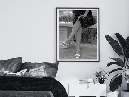 Framed black and white print of a person's legs in high heels on a wall above a bed.