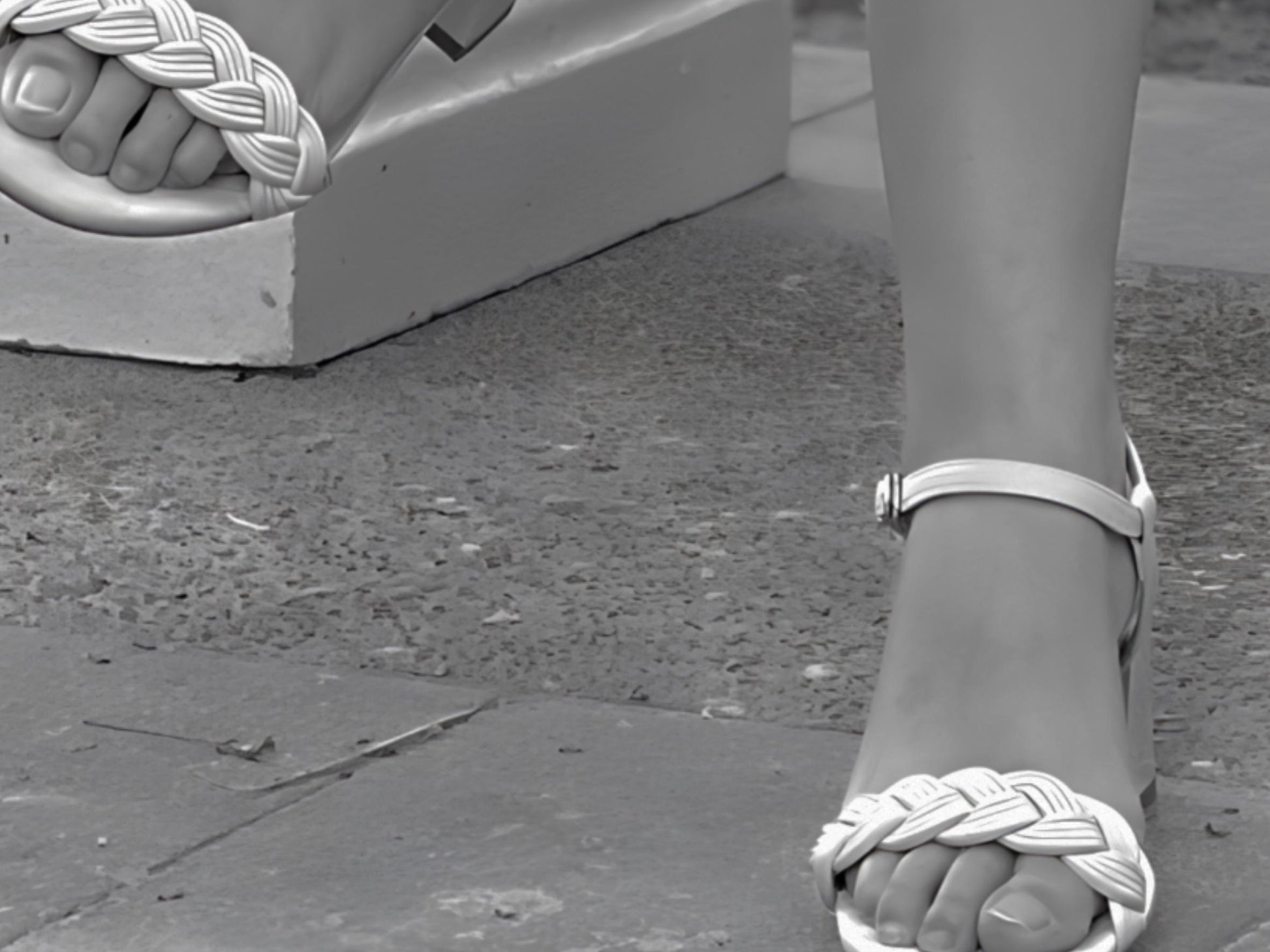 Close-up of a foot wearing a sandal with a woven design on a concrete surface.