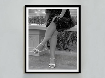 Framed black and white photograph of a person sitting outdoors wearing high heels.