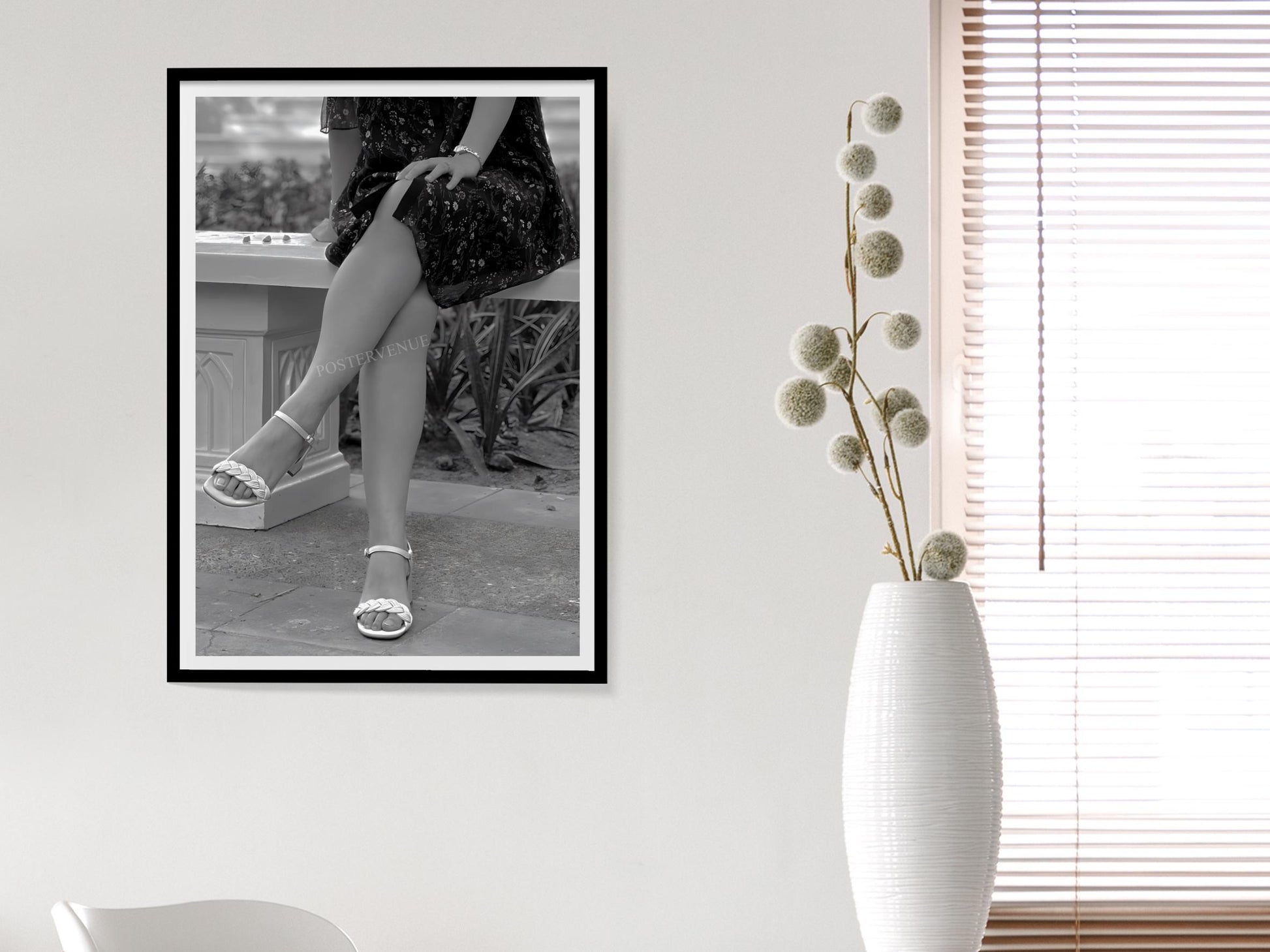 Framed black and white photo of a person in high heels on a wall next to a white vase with dried flowers.